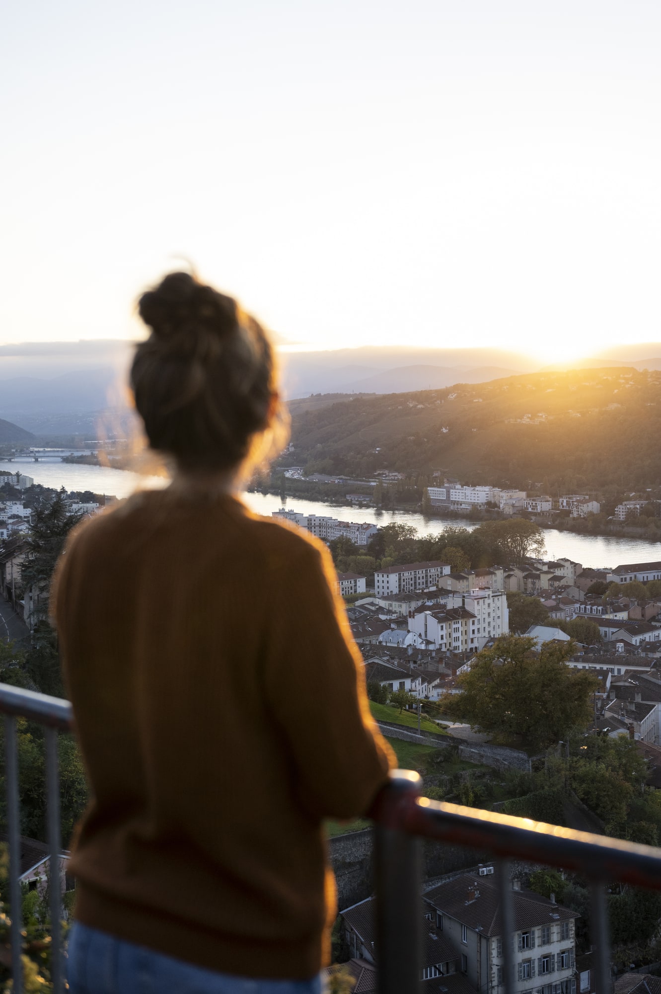 femme face au coucher du soleil surplombant une ville